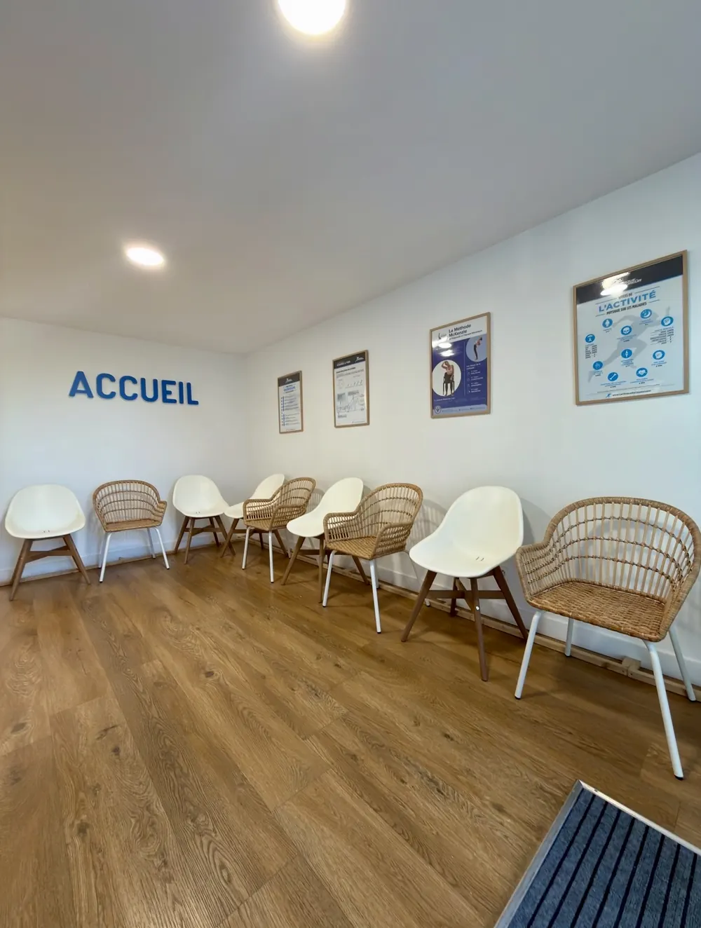 L'accueil du cabinet : le mot ACCUEIL peint en bleu sur le mur blanc, des chaises blanches et en rotin, des affiches