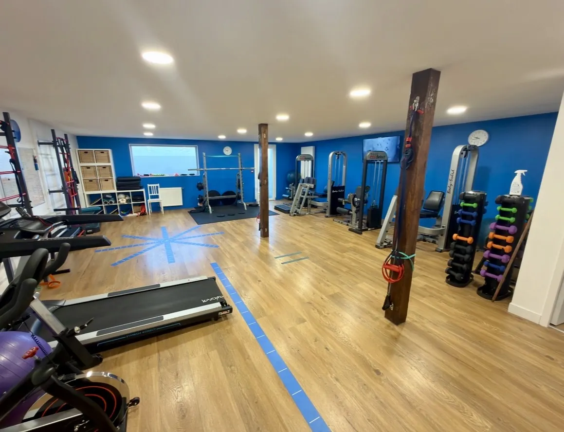 Le plateau de rééducation du cabinet : murs bleus, parquet, tapis de course, haltères et appareils de musculation